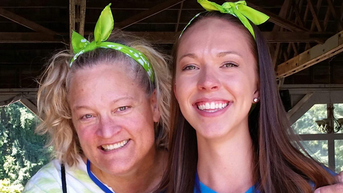 Two women side hugging looking at camera with matching green headbands