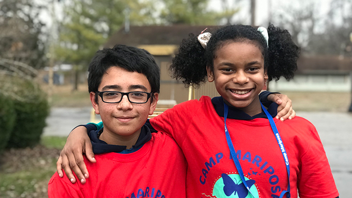 Two kids smiling at the camera in their red Camp Mariposa t-shirts