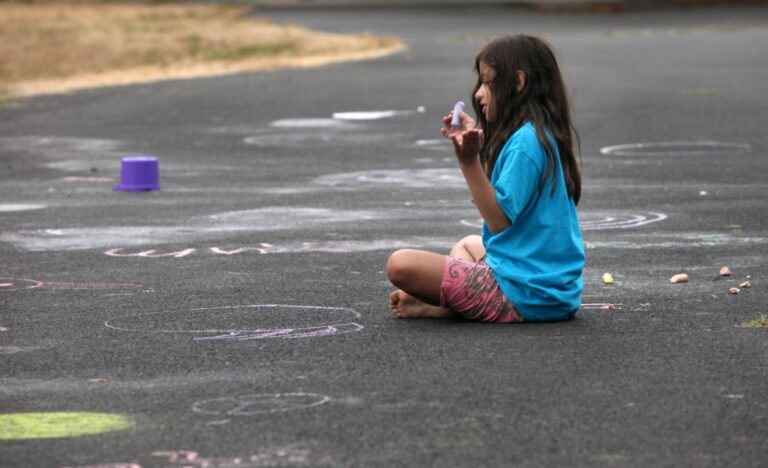 a child sitting alone on the pavement doing chalk drawings