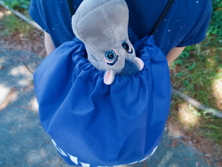 A emotional support stuffed hippo sticks its head out of an Eluna Care Package backpack