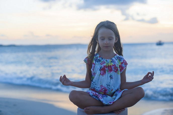 a child practices mindfulness on the beach with the ocean in the background