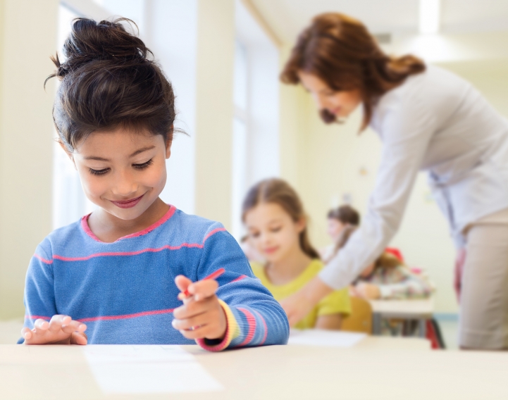 a child engaged in an activity is smiling while her educator is helping another child in the background