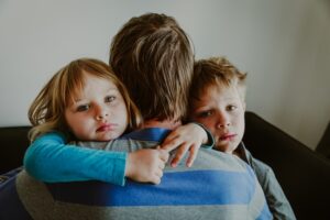 a father hugging his 2 children with his back to the camera