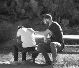 an adult comforting a child on a bench in black and white