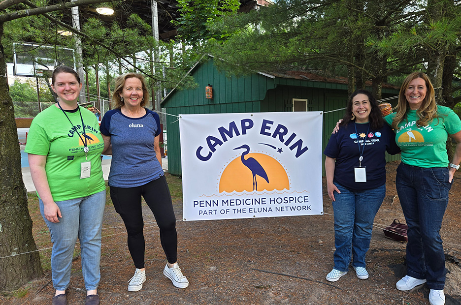 Four women standing on opposite sides of a camp erin sign.