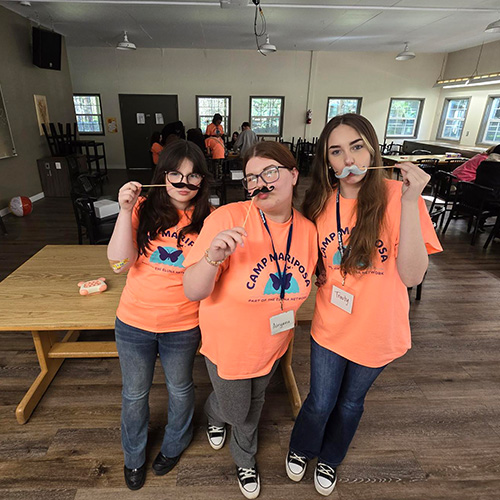 Three teenage girls holding up mustaches